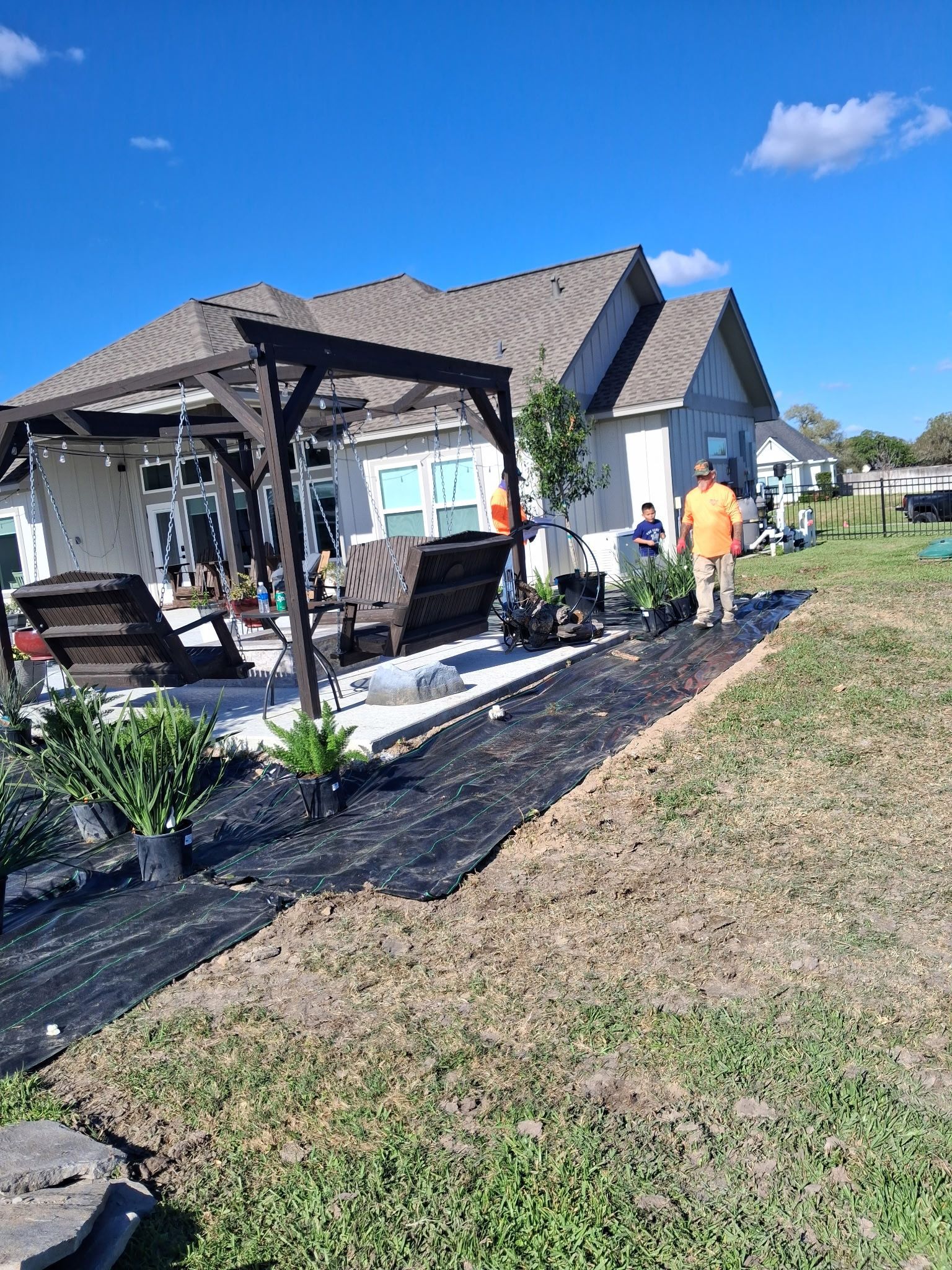 Damaged backyard gazebo with debris and two workers clearing the area under a sunny blue sky