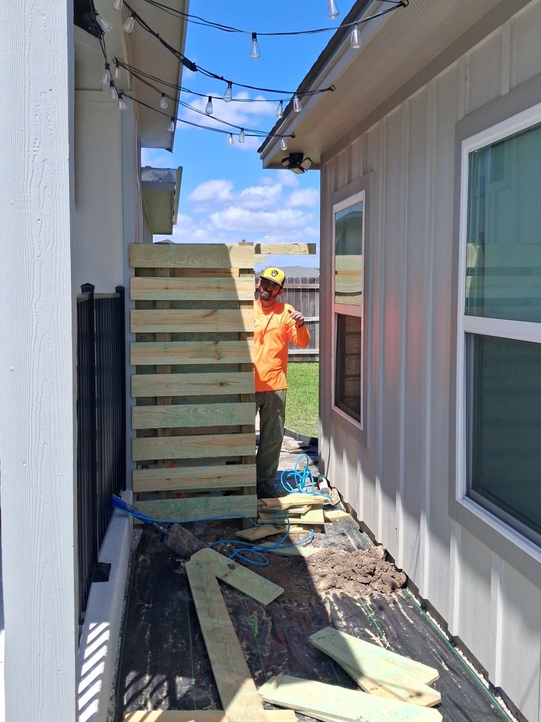 Worker in orange vest carrying stacked boards between two buildings on a narrow outdoor passage