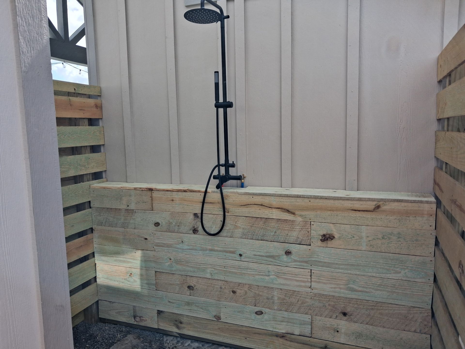 Small outdoor shower with wood slat walls and a hanging black showerhead fixture
