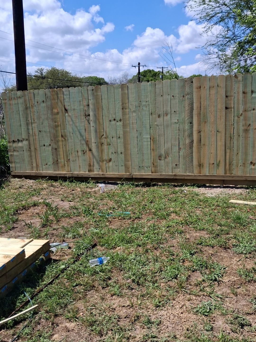 Weathered wooden fence along a grassy yard under a partly cloudy sky