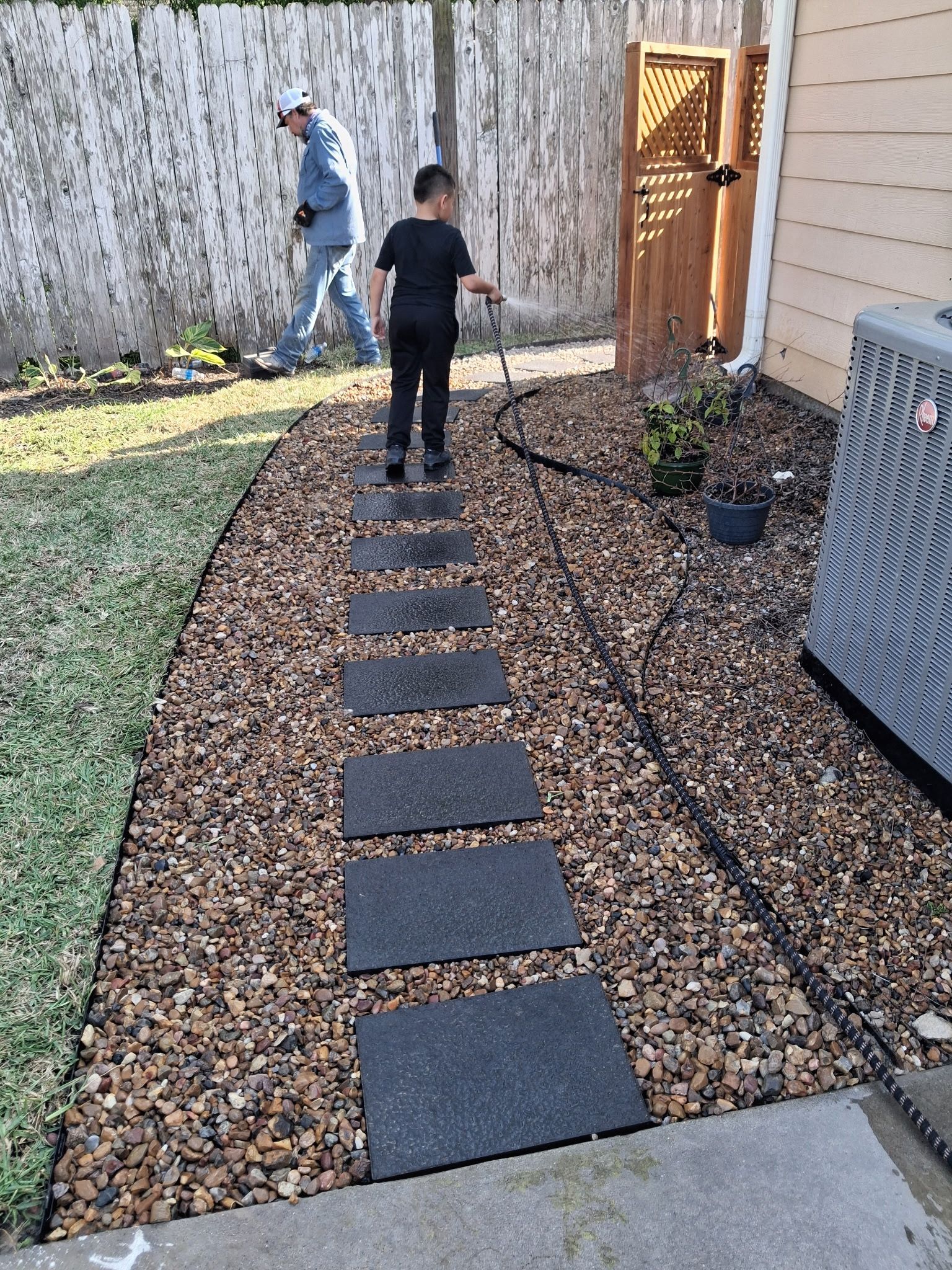 Stepping-stone path through gravel in a backyard, with two people near a wooden gate.