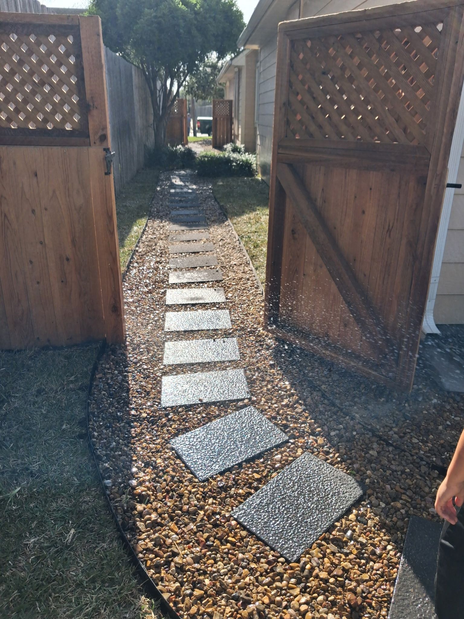 Stepping stone path through open wooden gate into a backyard garden