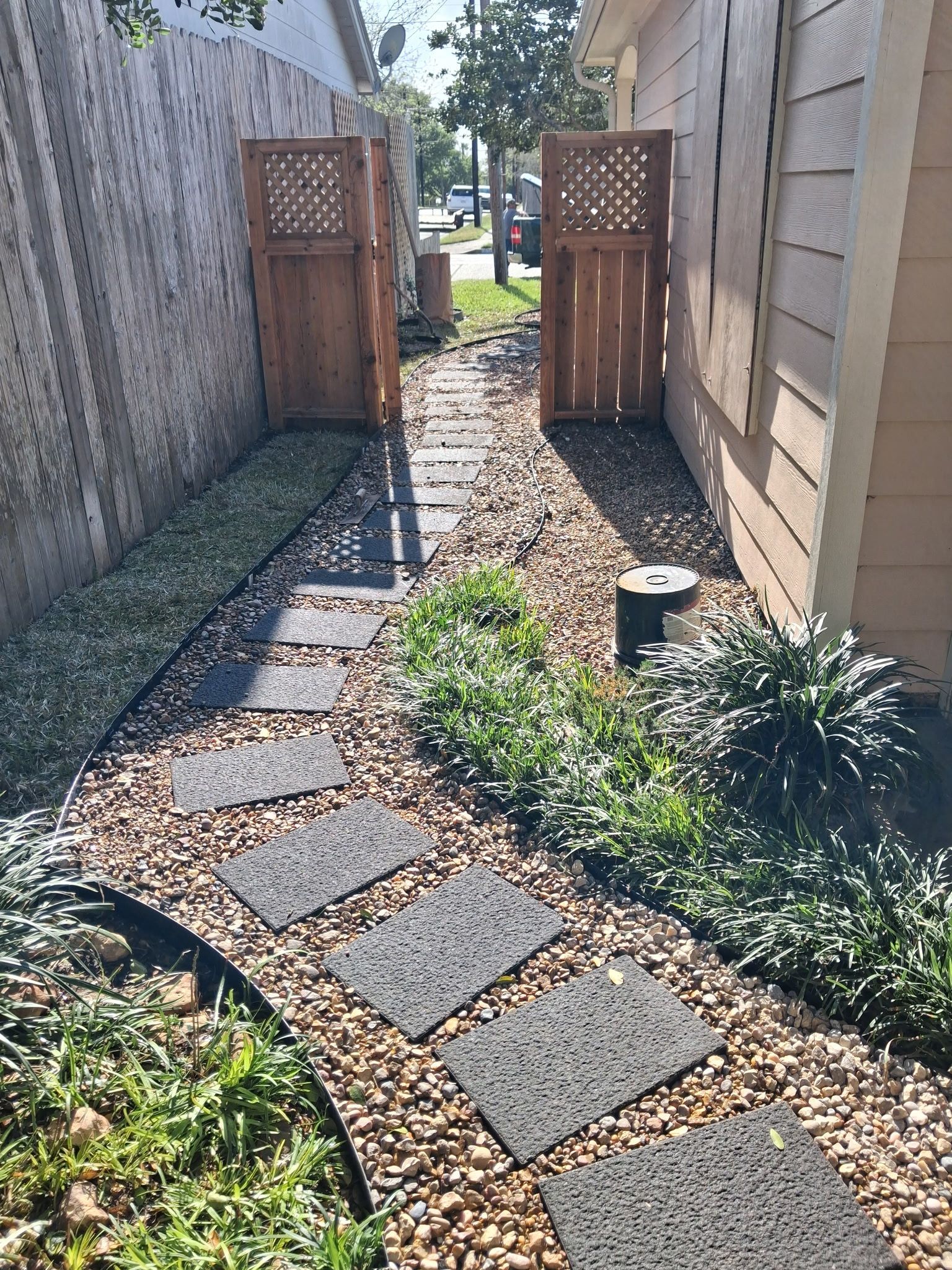 Narrow gravel garden path with stepping stones leading to a wooden gate between two buildings