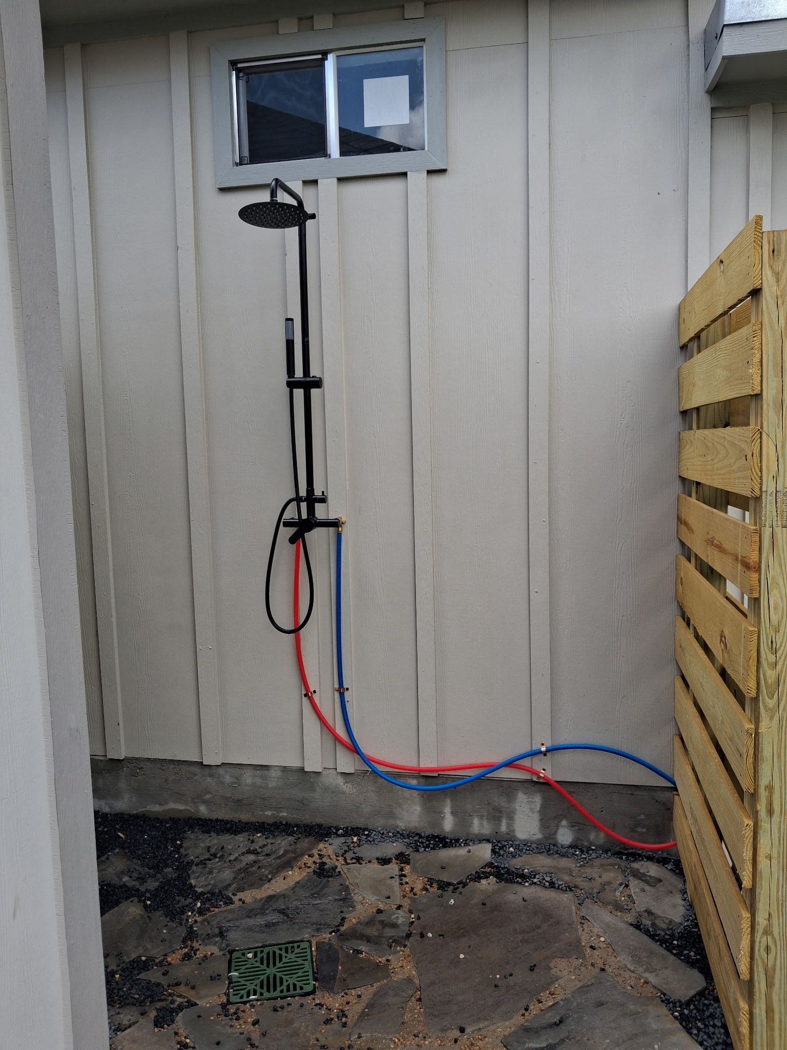 Blue and red hoses connected to a black tool hanging on a shed wall near a small window.