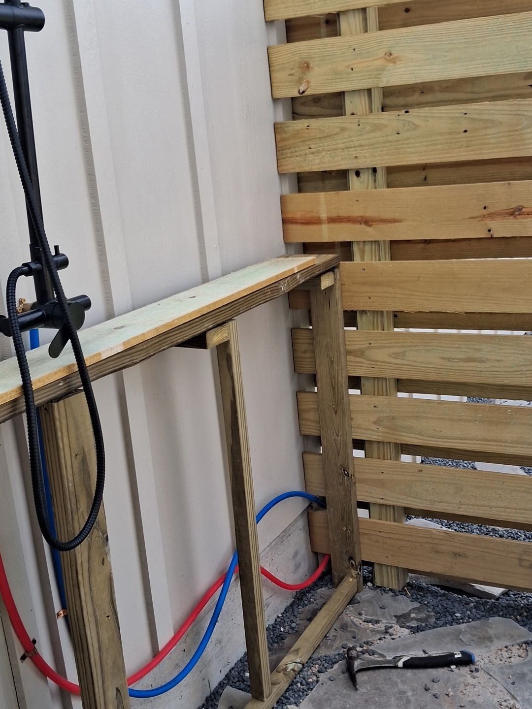 Partially built wooden wall frame with tools and blue-red hoses in a work area