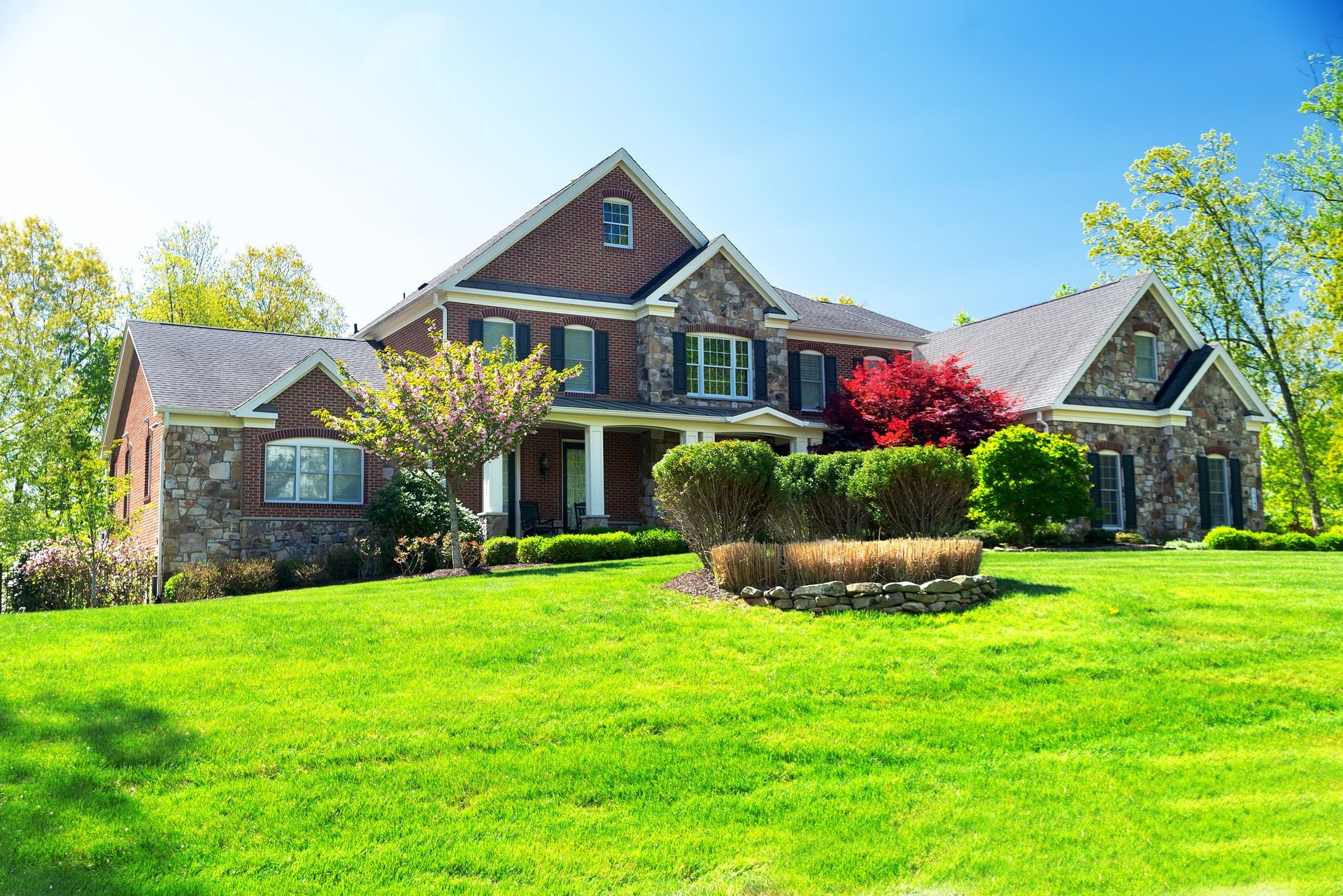 Large brick house with a manicured green lawn and bright blue sky