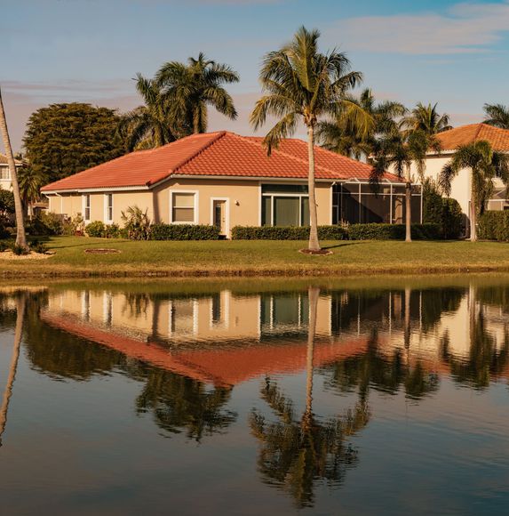 Tropical house with red roof and palm trees reflected in a calm pond