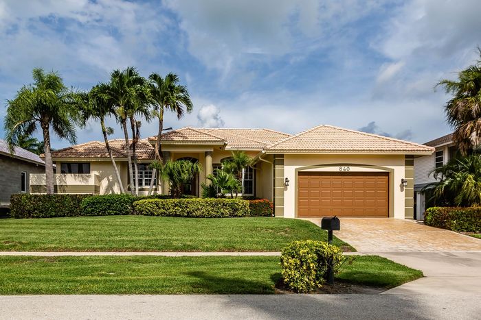 Single-story suburban house with tiled roof, garage, palm trees, and manicured lawn