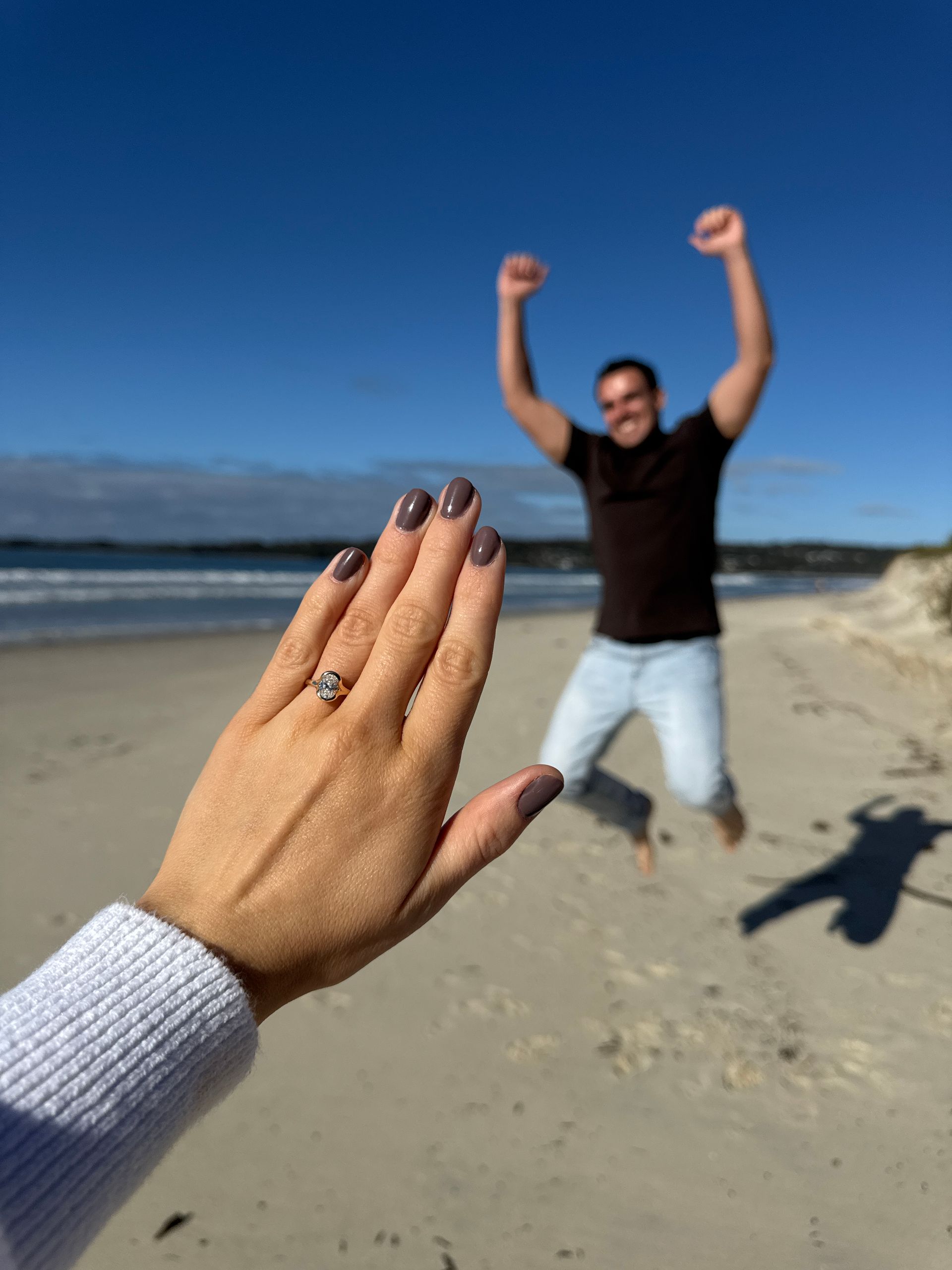 Chloes hand reaching toward a  Nick cheering on a sunny beach under a clear blue sky