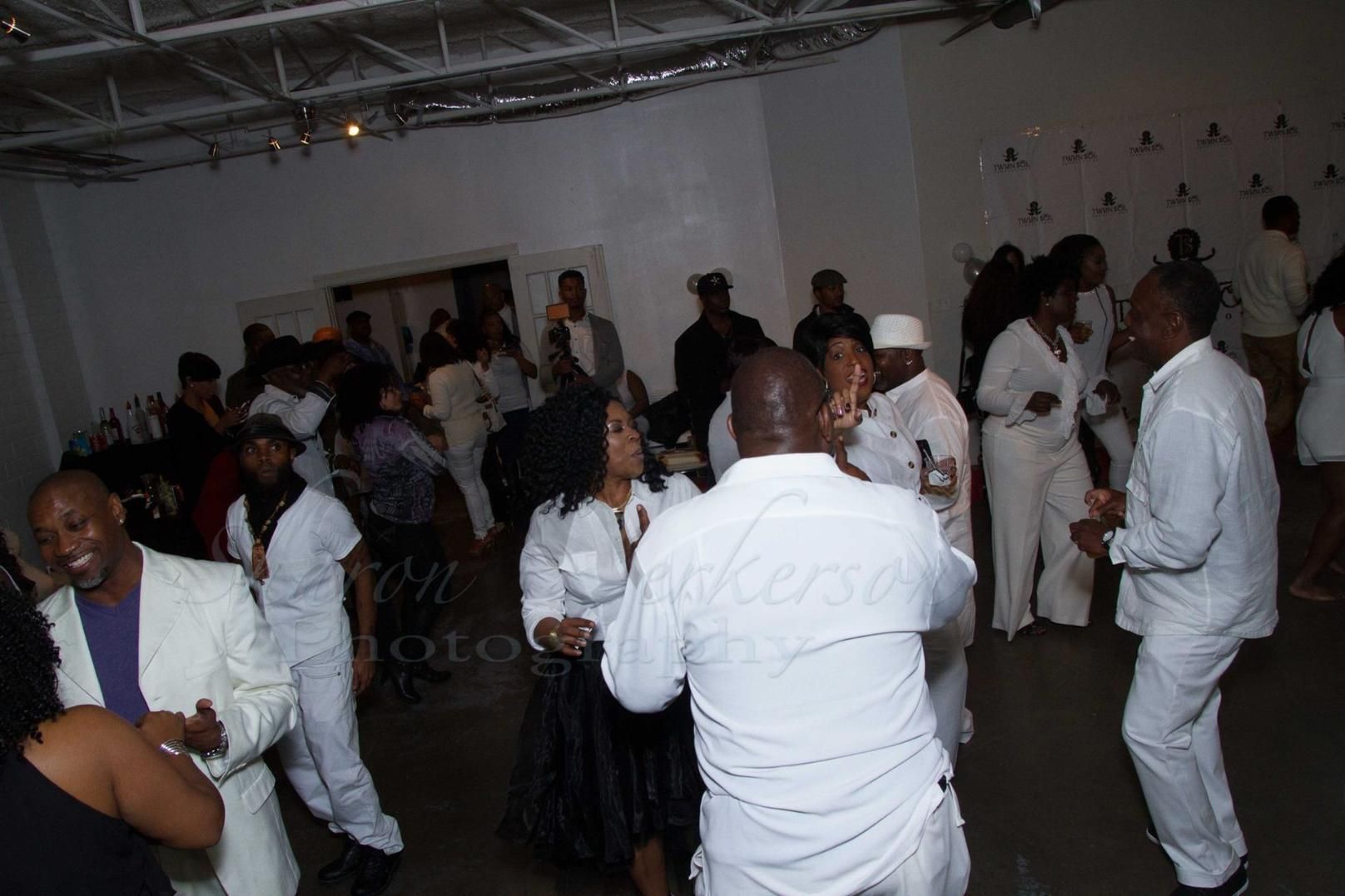 People dancing and mingling at an indoor party, with white walls and dim lighting.