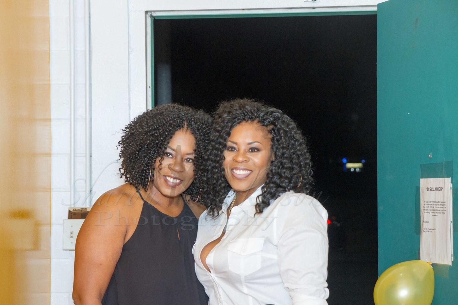 Two smiling people standing together indoors in front of an open doorway.