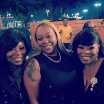 Three smiling people posing together outdoors at night, with lights and a crowd in the background.