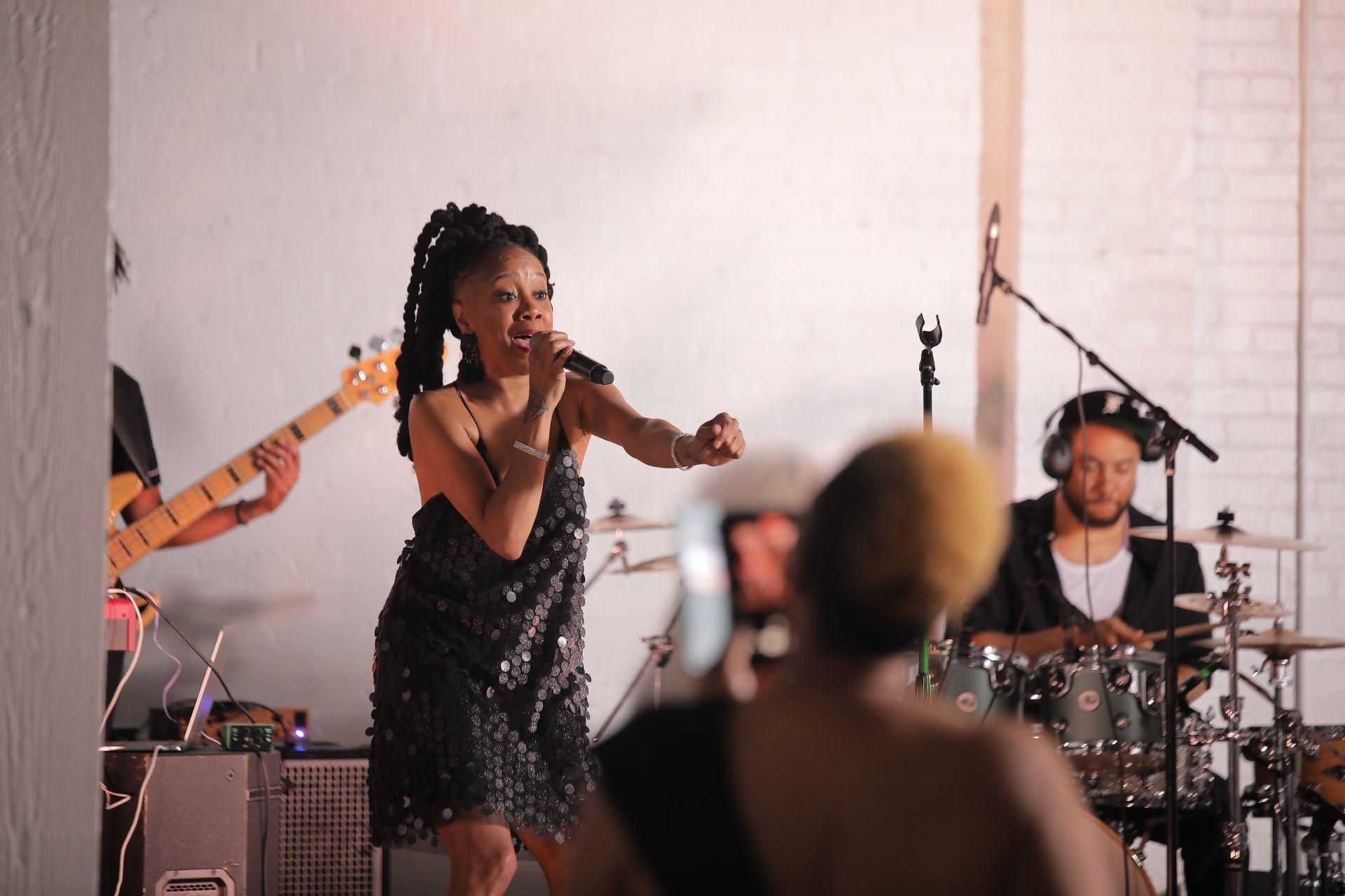 Singer performing on stage with drummer and guitarist in the background