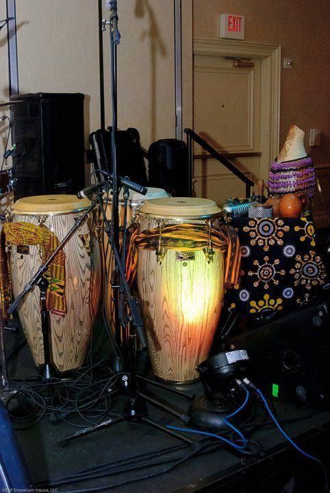 Two conga drums and microphone stands on a stage, with a decorative drum and speaker nearby.