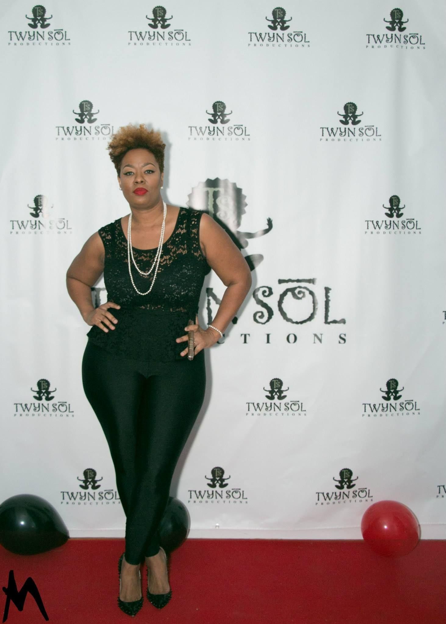 Woman posing in a black dress at a step-and-repeat event backdrop with balloons