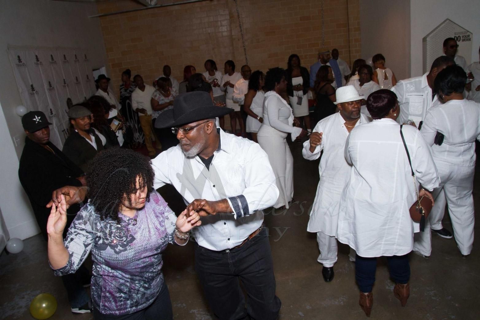 People dancing at a lively indoor party, with a couple in the foreground and others mingling behind them.