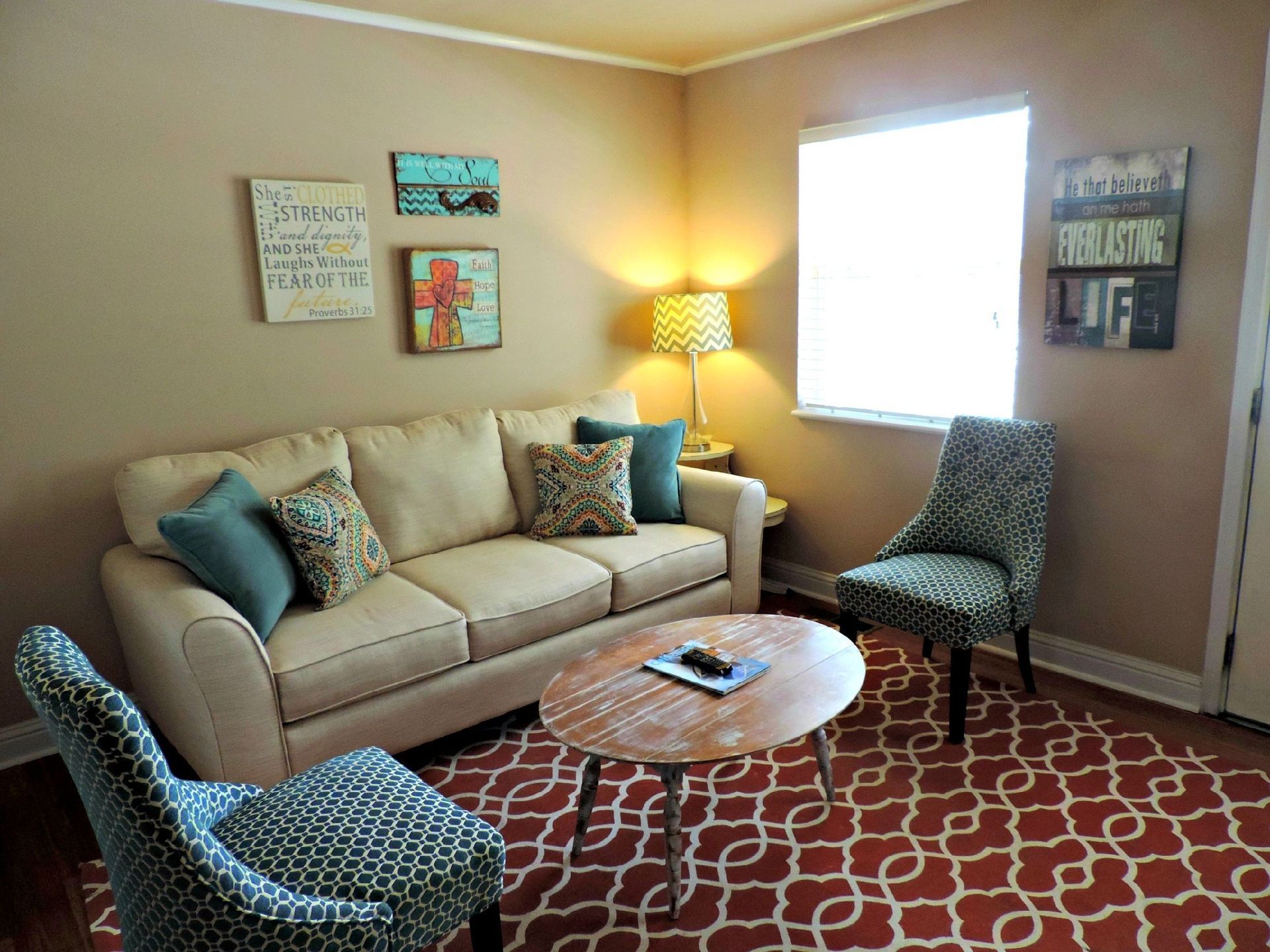 Cozy beige living room with patterned chairs, sofa, red rug, lamp, and bright window