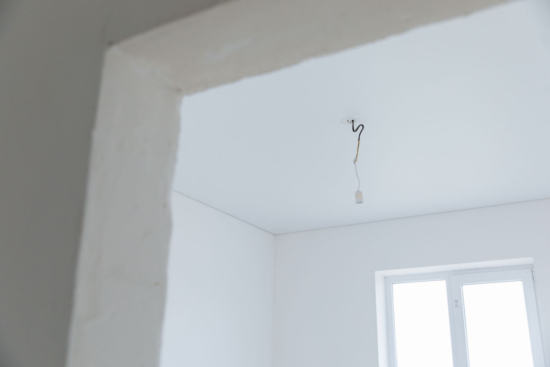 White room interior with a ceiling light wire hanging near a window and doorway opening.