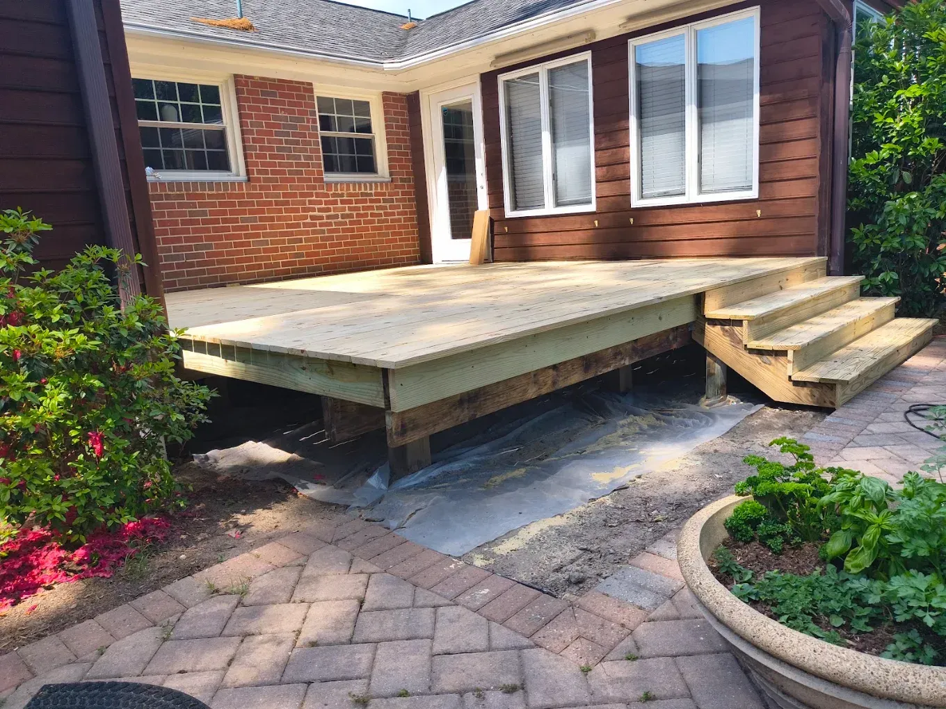 Backyard wooden deck with steps, beside a brick house and brick patio garden.