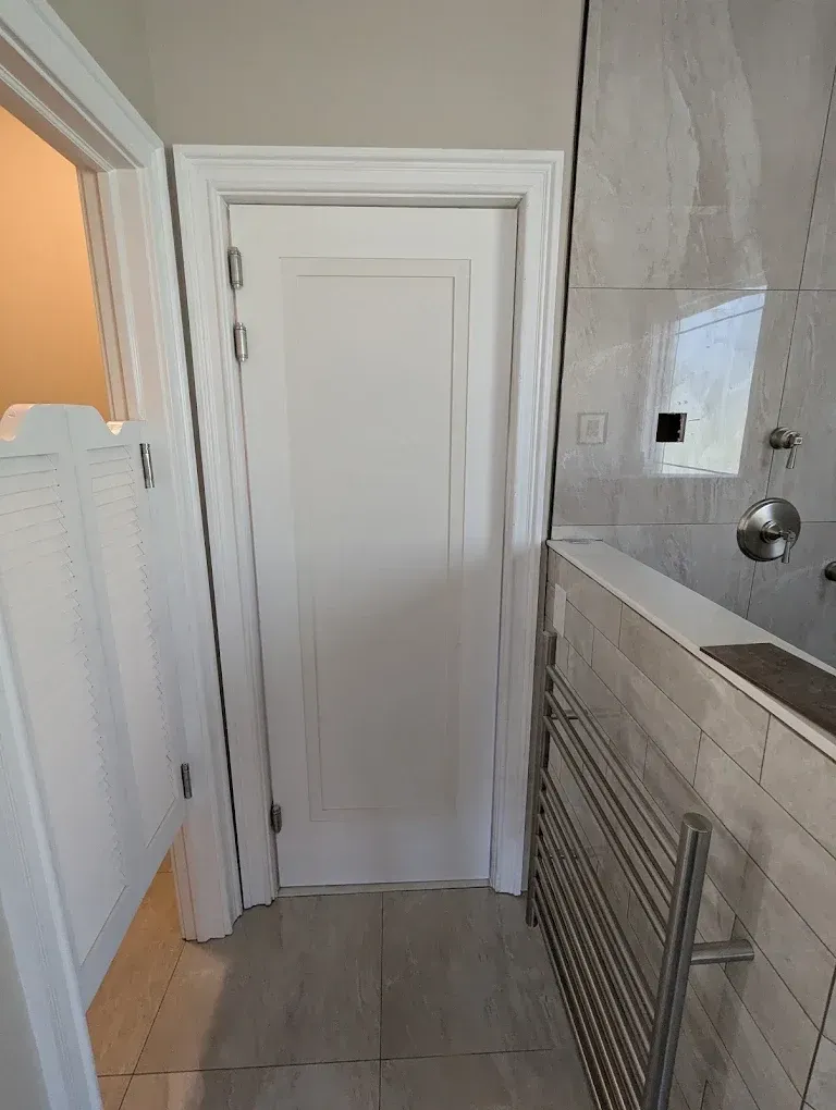 Narrow bathroom hallway with white door, tiled floor, and vanity/counter on the right.