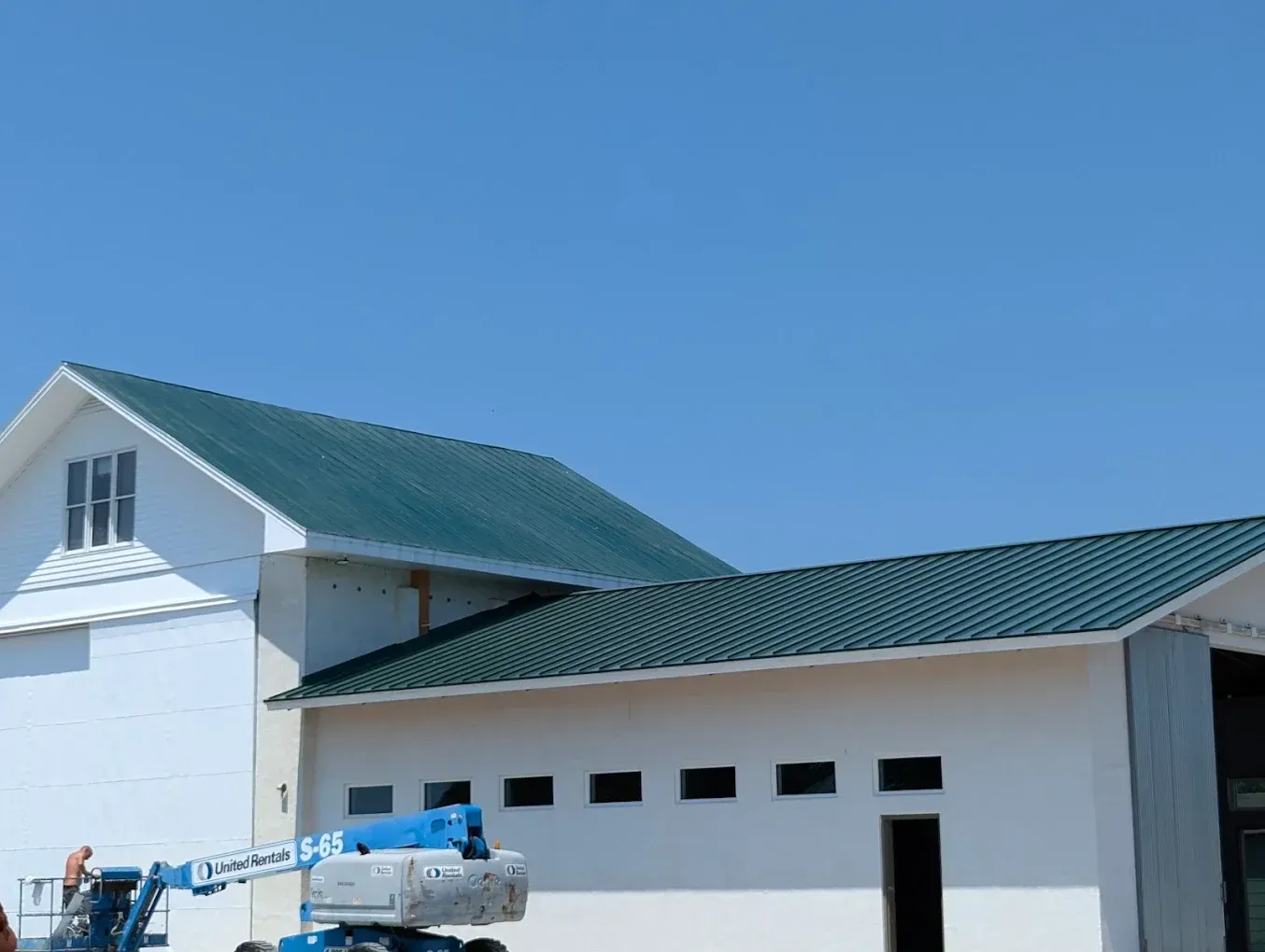 White building with green roof under blue sky, with a truck lift parked beside it.