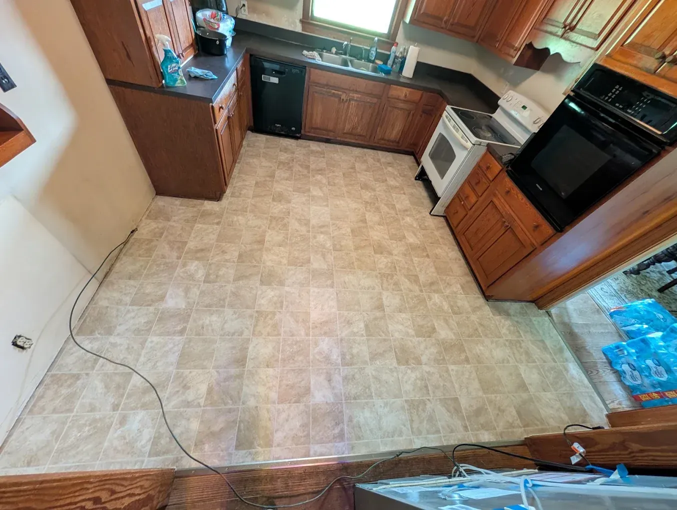 Empty kitchen with tan tile floor, wooden cabinets, and a window over the sink.
