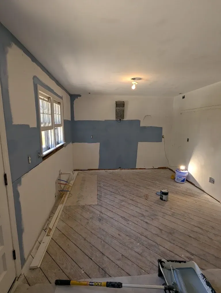 Partially painted room with gray-blue walls, white ceiling, and bare wood floor during renovation
