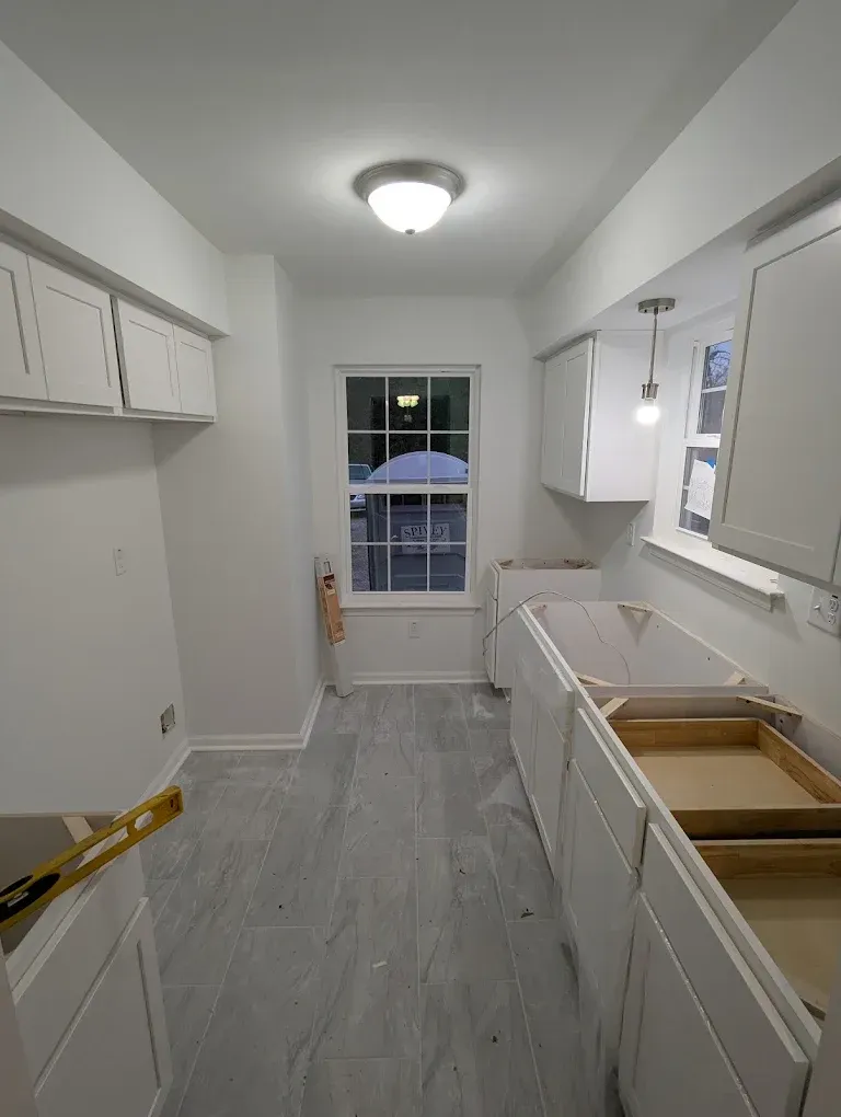 Bright white galley kitchen under renovation with unfinished cabinets and countertop near a back door.