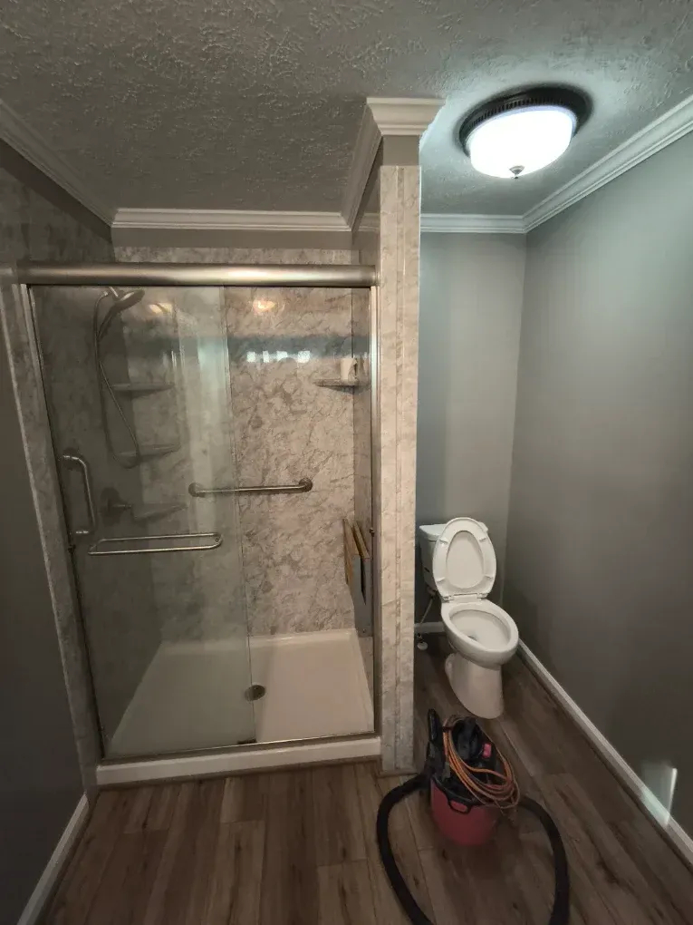 Bathroom with a shower stall, toilet, and ceiling light, featuring gray walls and wood-pattern flooring.
