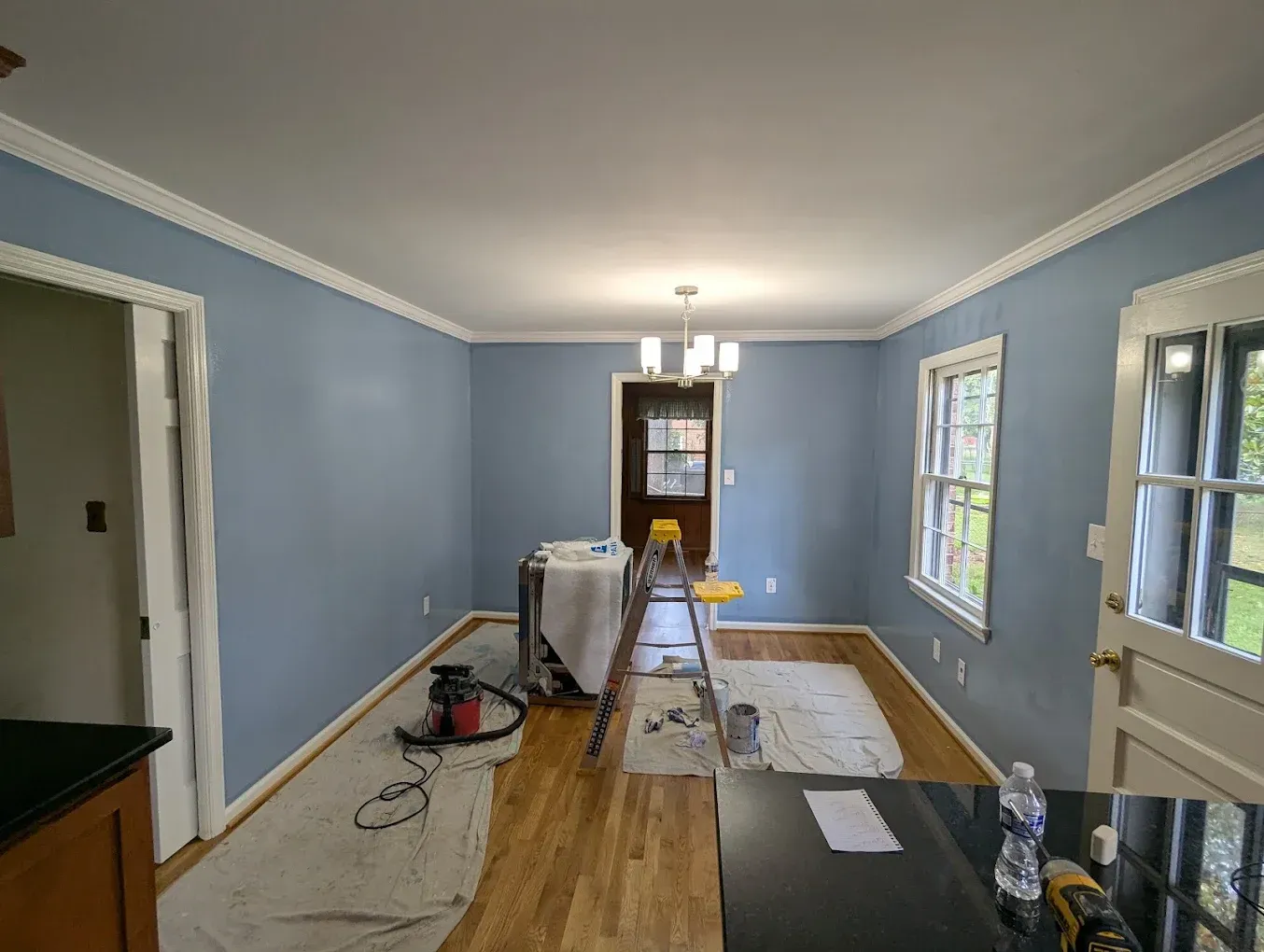 Blue-walled room under renovation with ladder, tools, and floor coverings.
