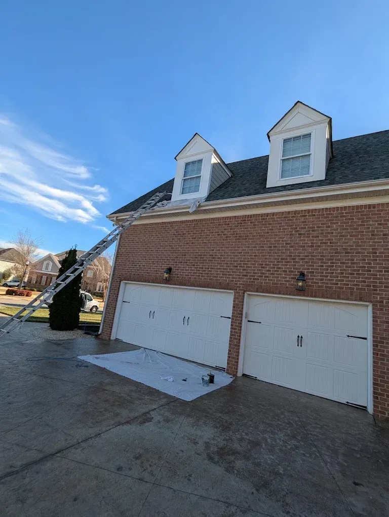 Brick house with two white garage doors and dormer windows under a blue sky