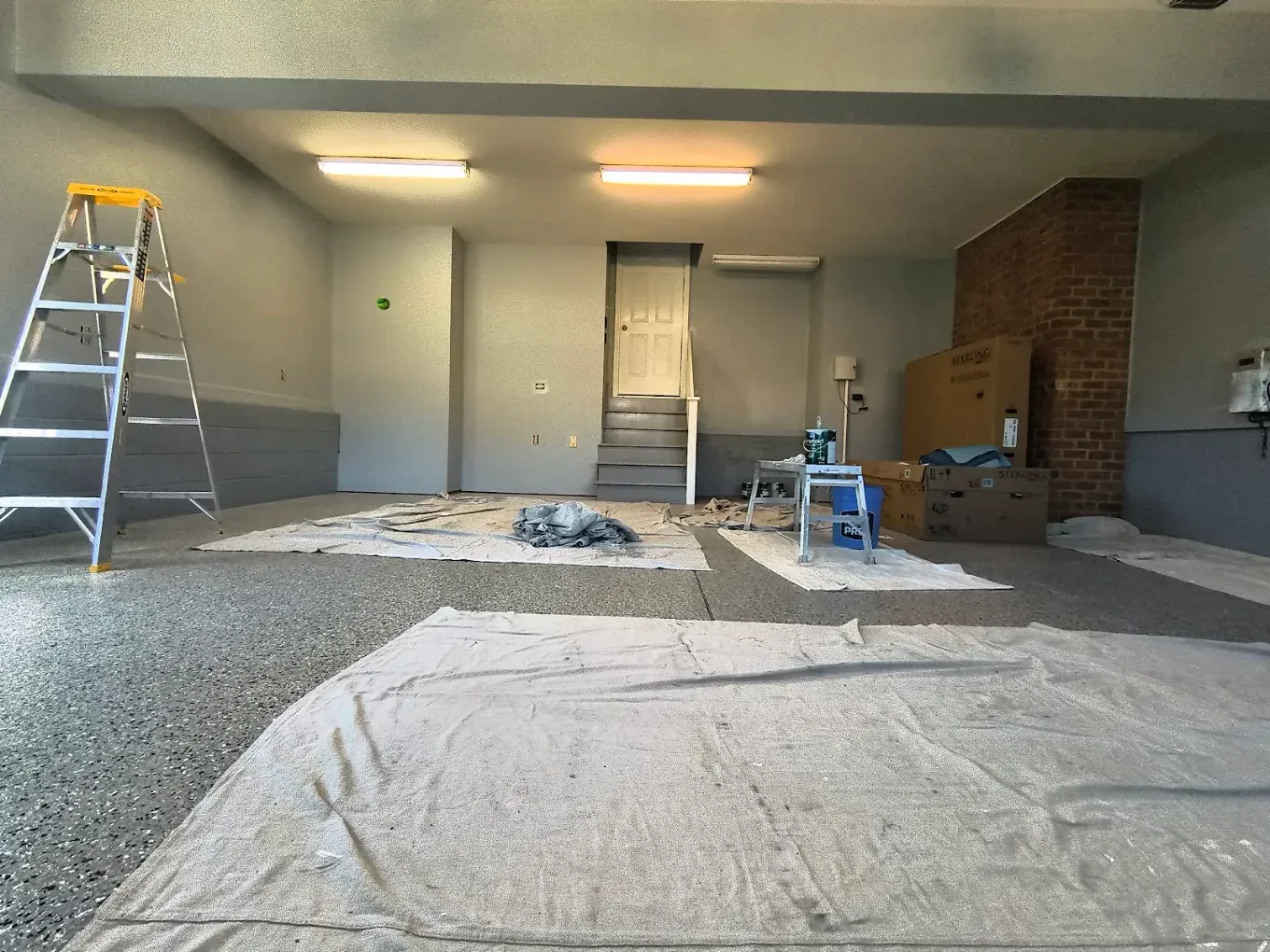 Partially covered garage with ladder, paint supplies, and a brick wall under renovation