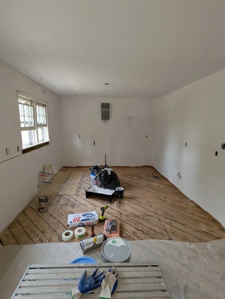Empty room under renovation with exposed floorboards and scattered tools on a tarp.