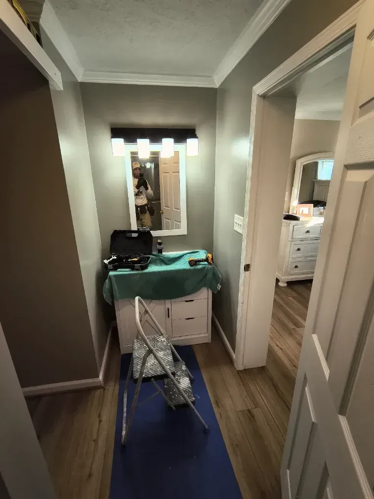Narrow hallway with a vanity, mirror, clothing rack, and blue runner rug leading to a bright room.