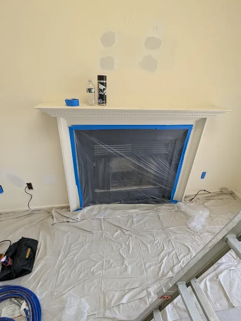 Room under renovation with a blue-taped fireplace, drop cloth on the floor, and tools scattered nearby