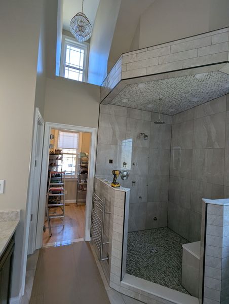 Tall unfinished interior with a tiled shower, high window, and doorway to a hallway with a ladder.