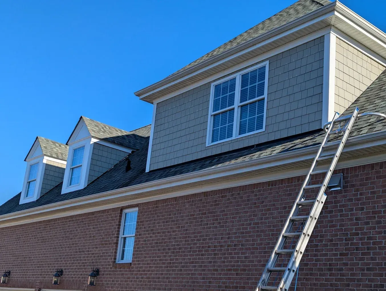 Brick house with dormer windows and a ladder leaning against the roof under a blue sky
