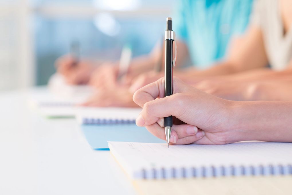 Mani che scrivono con penne su carta in un'aula luminosa o in una sala riunioni.