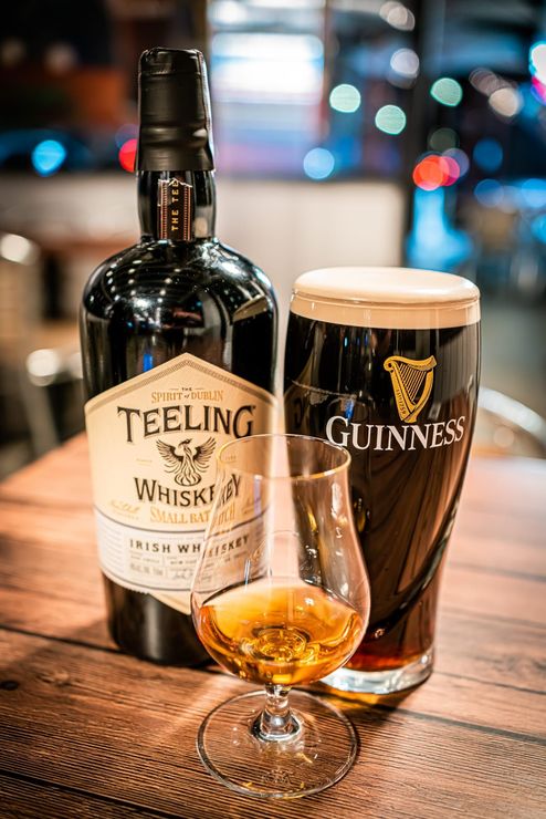 Teeling whiskey bottle, Guinness pint, and whiskey glass on a wooden table in a bar setting