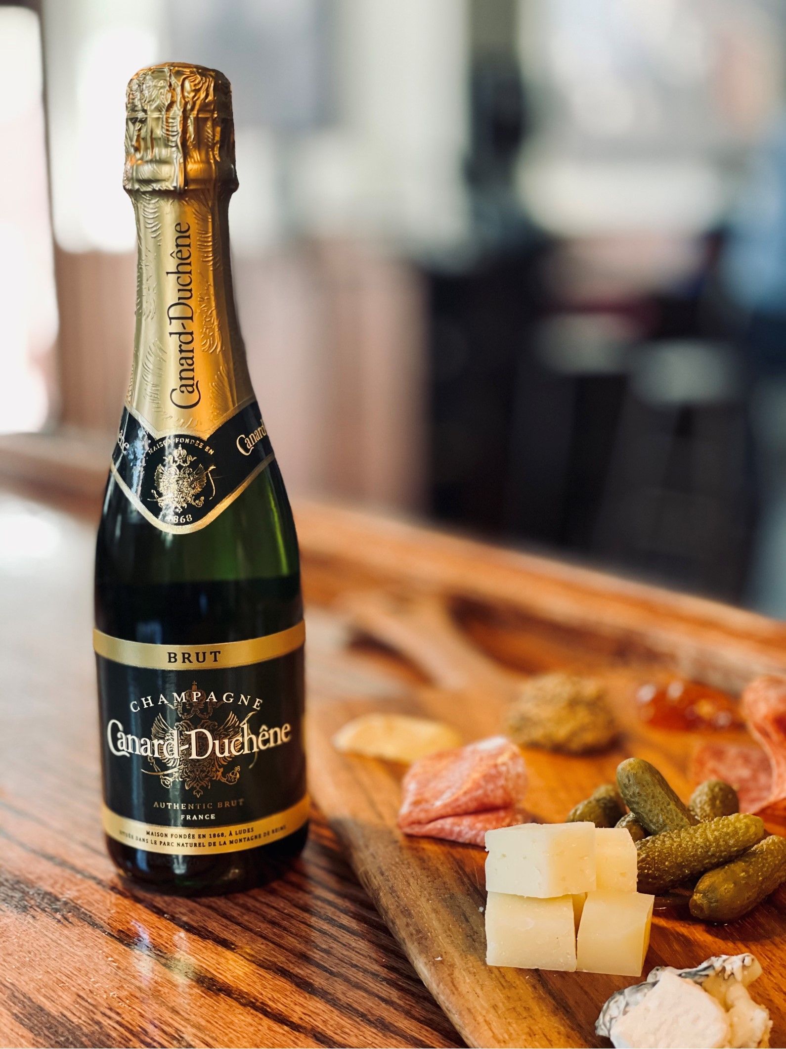 Champagne bottle beside cheese and charcuterie on a wooden table
