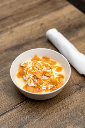 Small bowl of creamy orange dessert topped with crumbs on a wooden table next to a rolled white napkin
