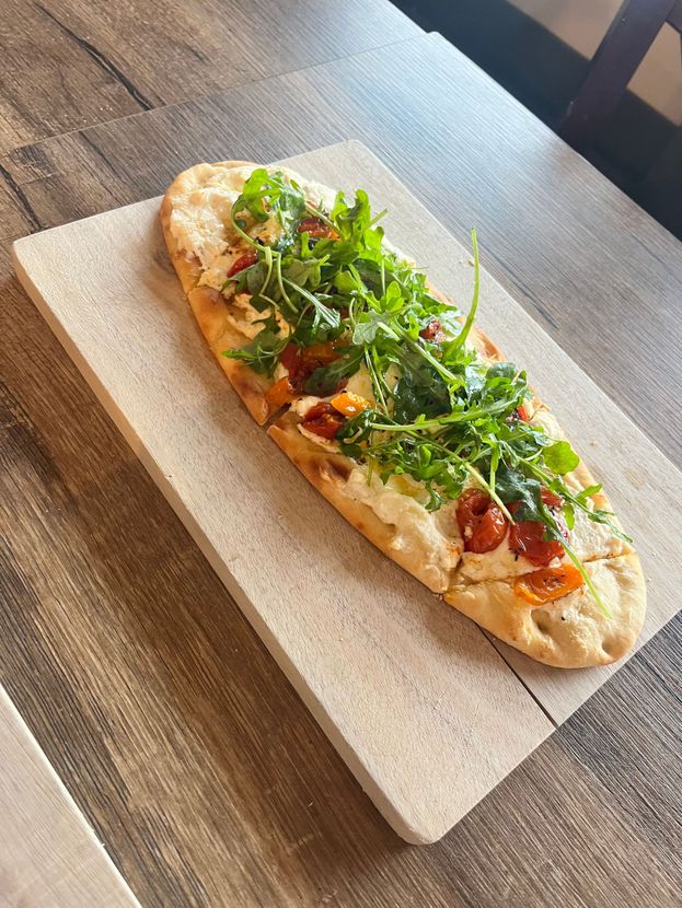 Flatbread pizza topped with greens and cherry tomatoes on a wooden serving board