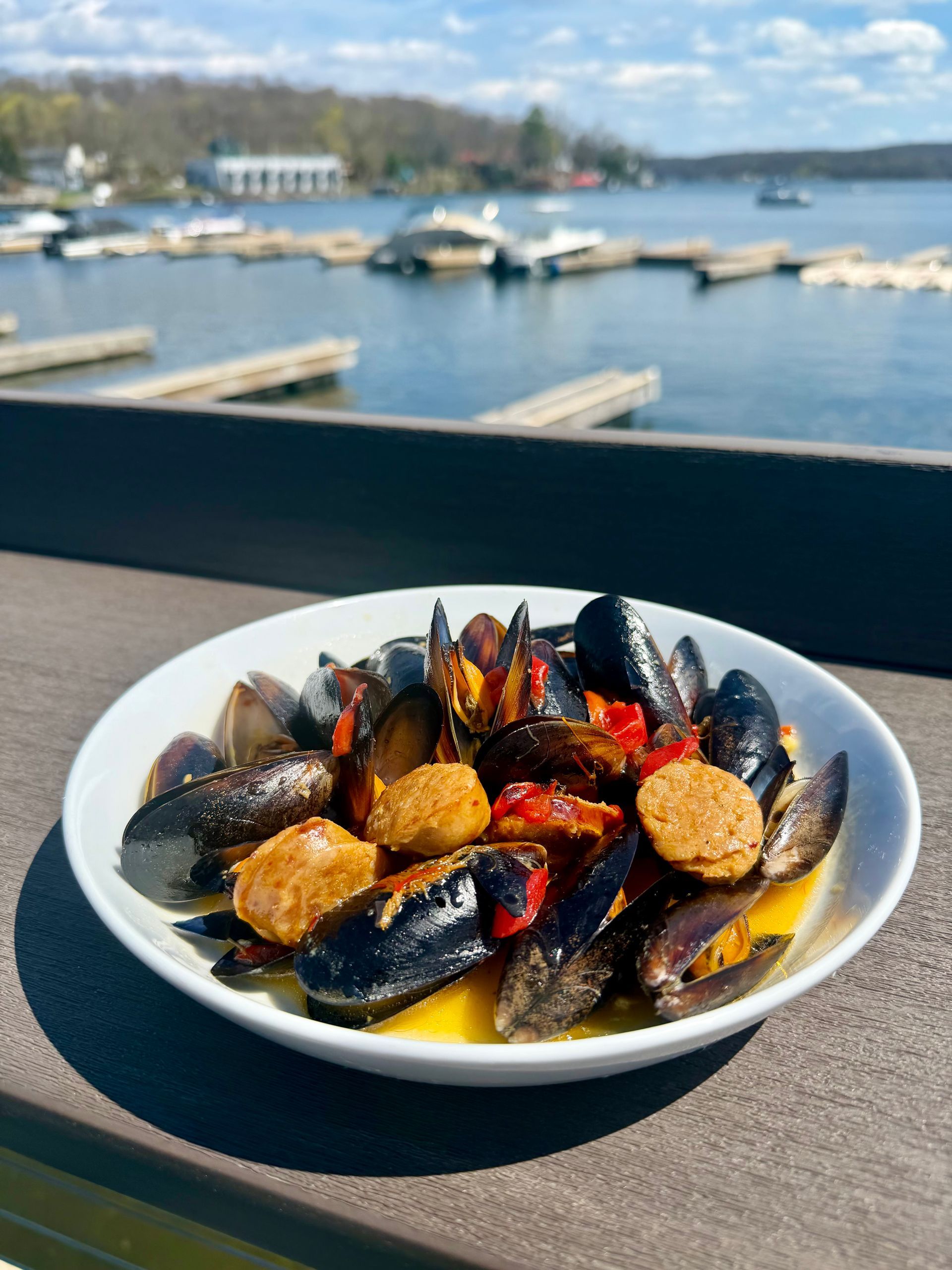 Seafood stew in a white bowl on a table, with a marina and boats in the background
