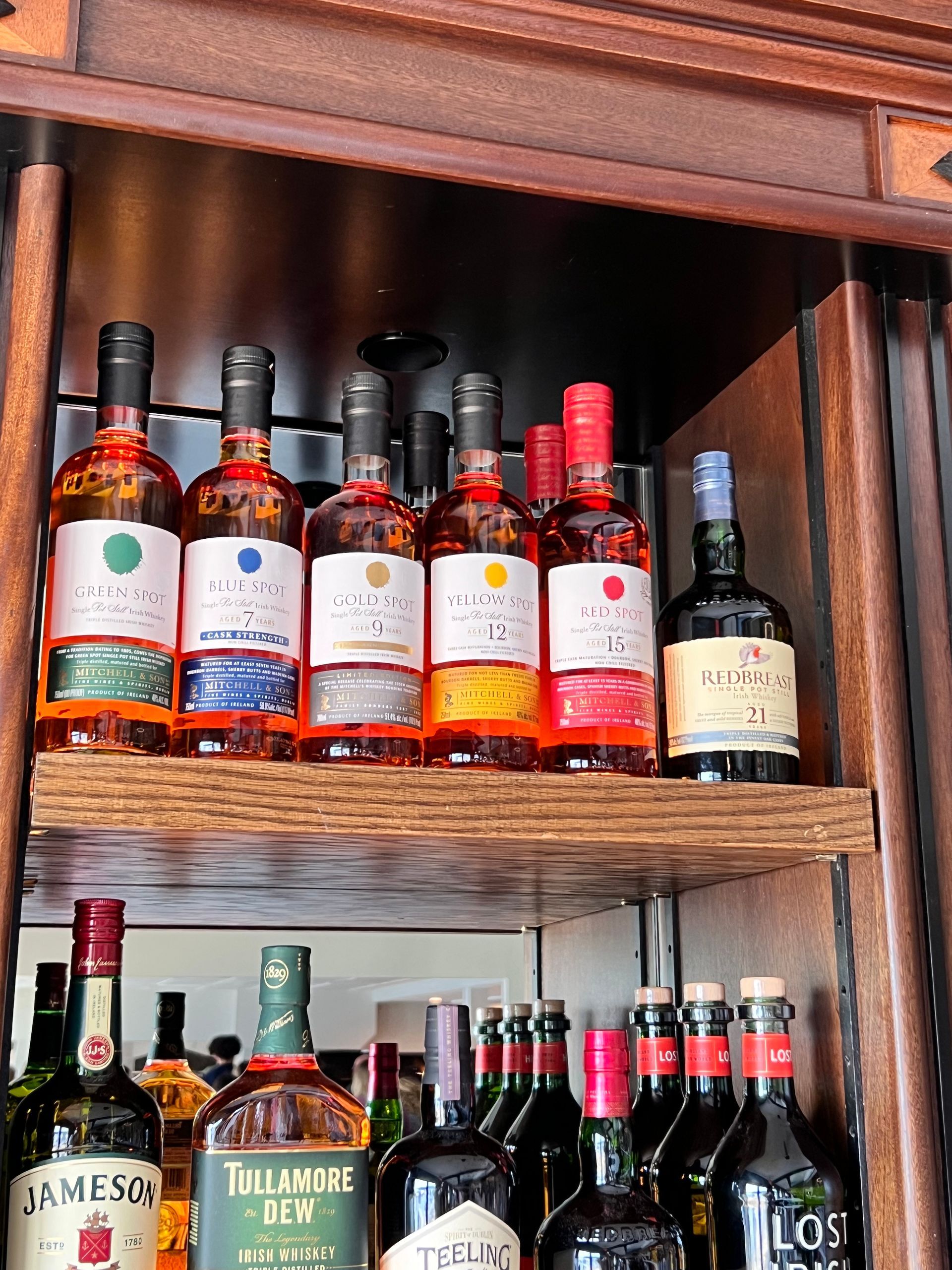 Shelves of assorted wine and liquor bottles in a wooden cabinet, with colorful labels and dark glass bottles