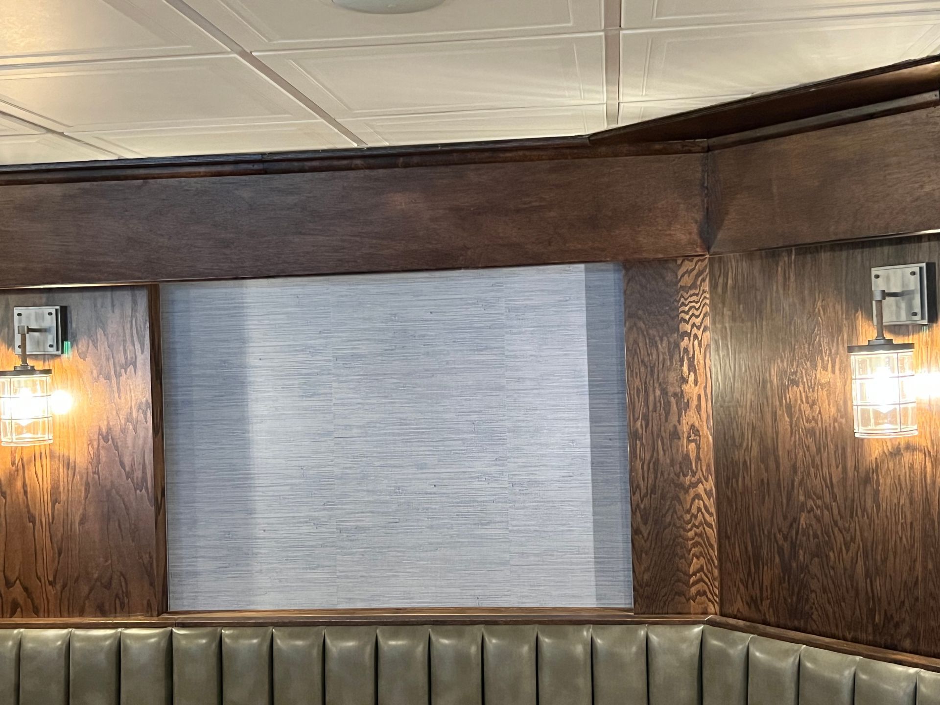 Wood-paneled wall with two lit sconces and a gray window shade above a padded bench seat