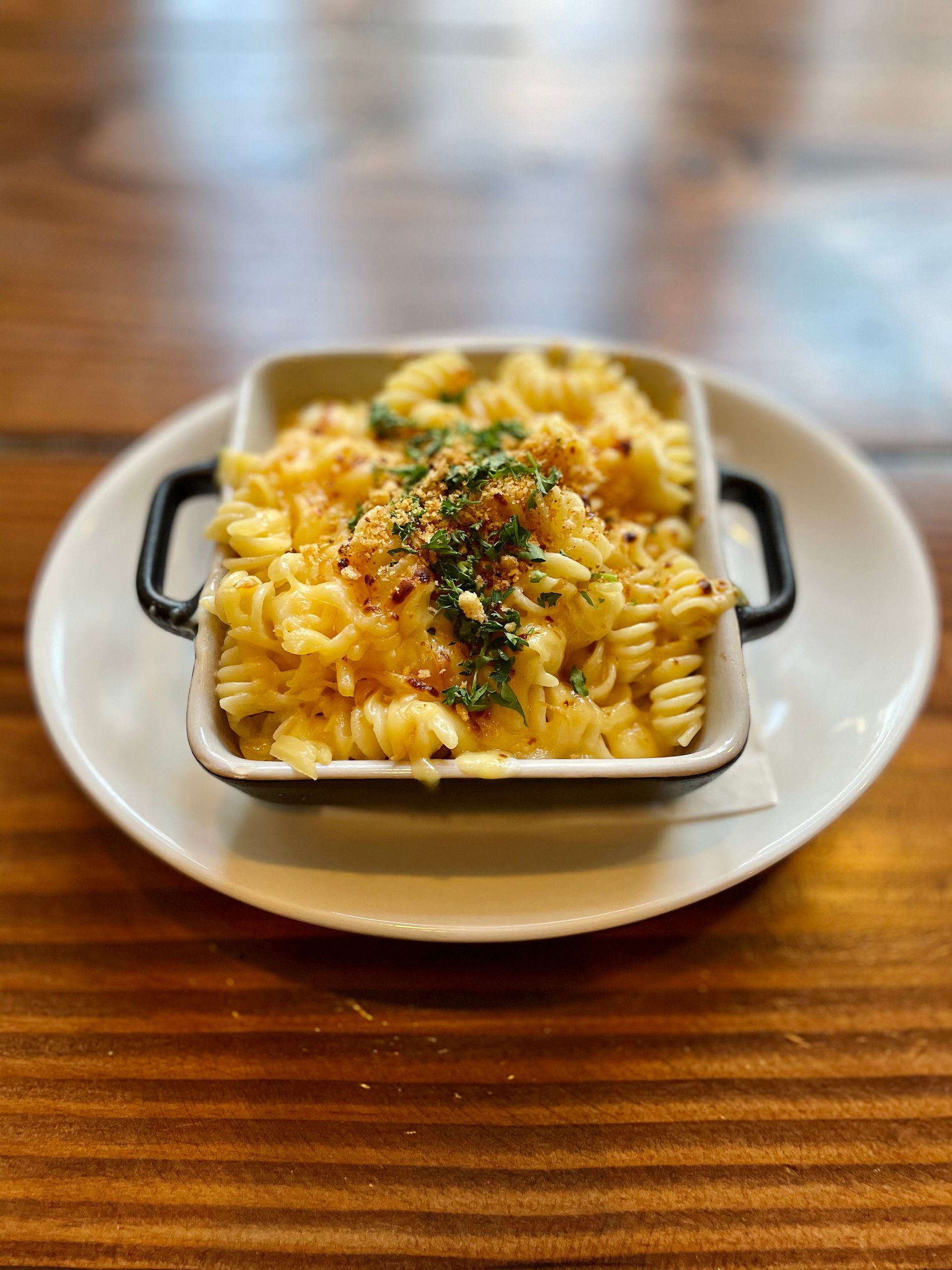 Baked pasta casserole in a white dish on a plate, topped with herbs on a wooden table