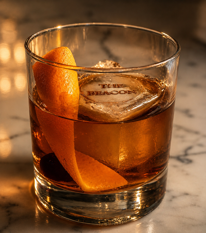 Whiskey on the rocks in a low glass with an orange peel garnish on a marble surface