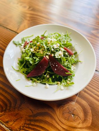 Mixed green salad with beet slices and grated cheese on a white plate on a wooden table