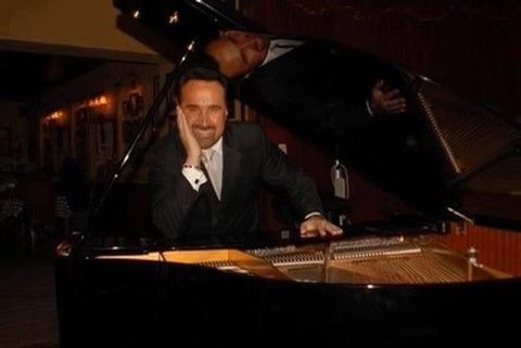 Man smiling at a grand piano in a warmly lit room, with the lid raised