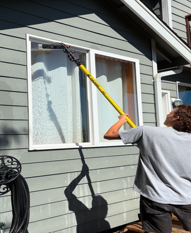 A professional worker wearing blue gloves is performing residential window cleaning services.